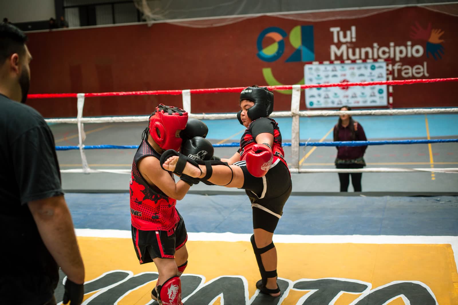 Dos kickboxers haciendo sparring con casco y espinilleras sobre el ring