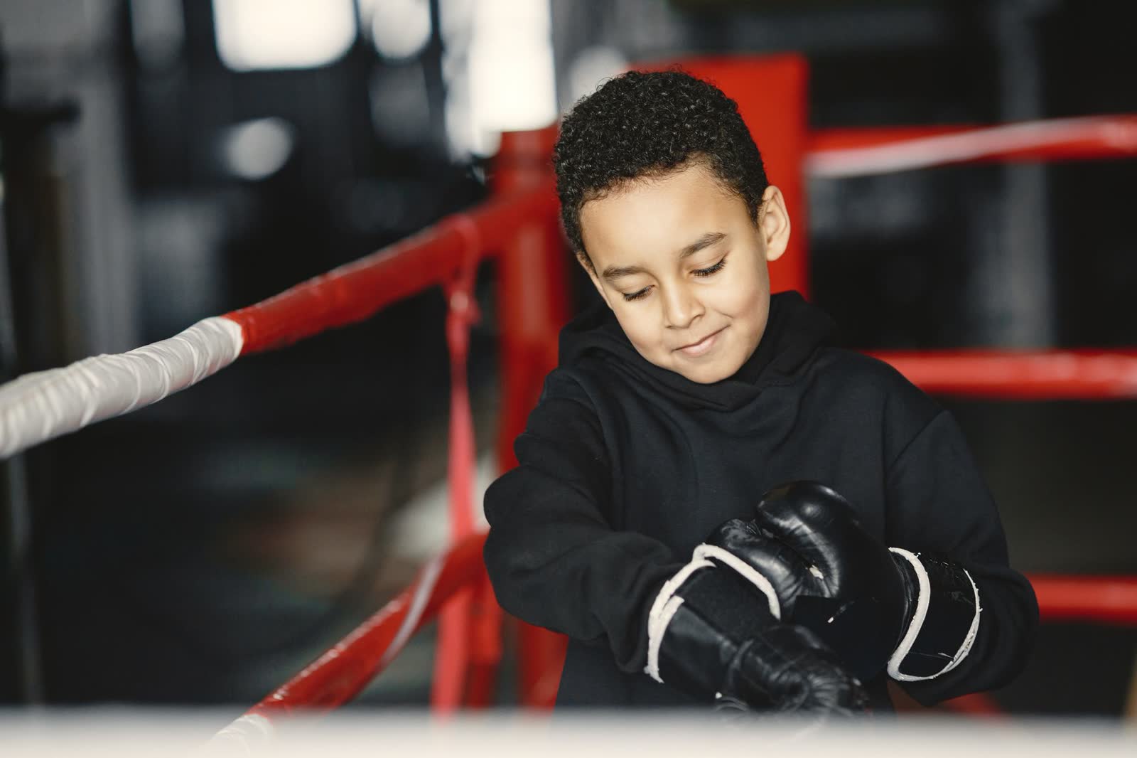 Niño ajustándose los guantes en el ring, sonriendo antes de la clase